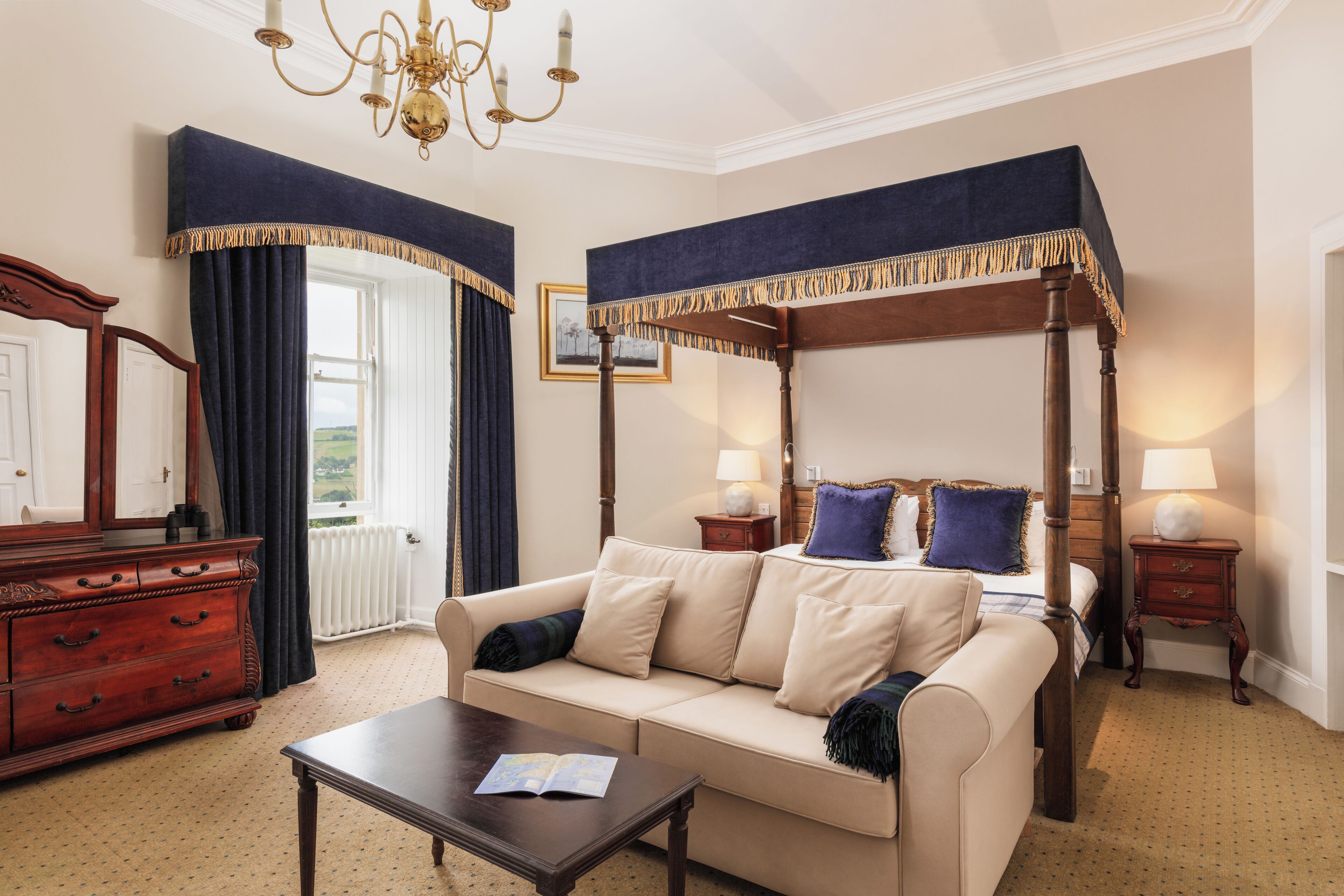 A bedroom with a four-poster bed, a sofa, a wooden dresser, and a chandelier.