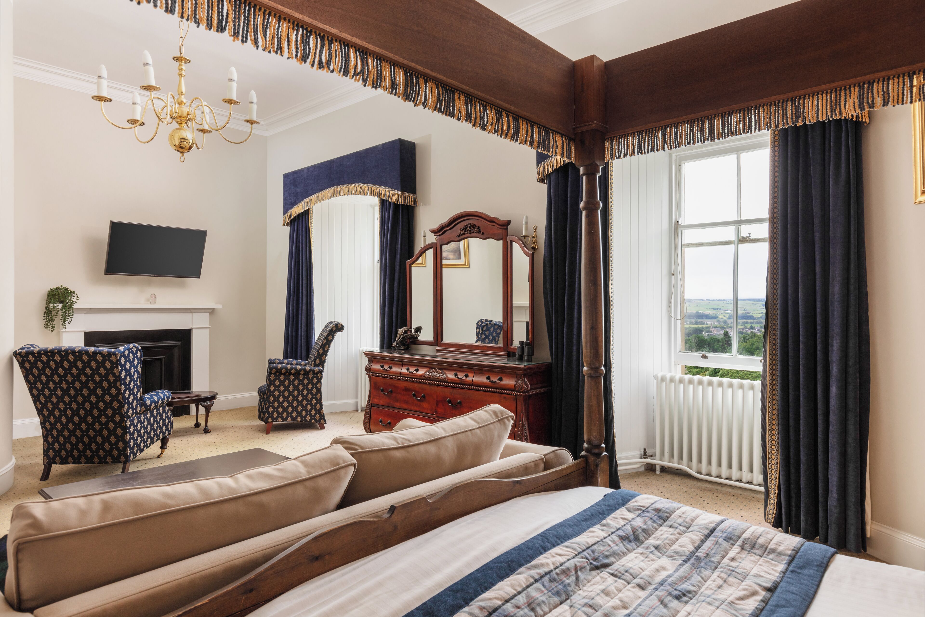 Een slaapkamer met een groot bed, een dressoir, een spiegel, een televisie en een open haard.