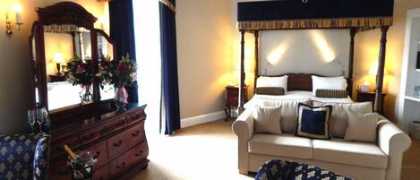 A bedroom with a four-poster bed, a dresser, a sofa, and a chandelier.