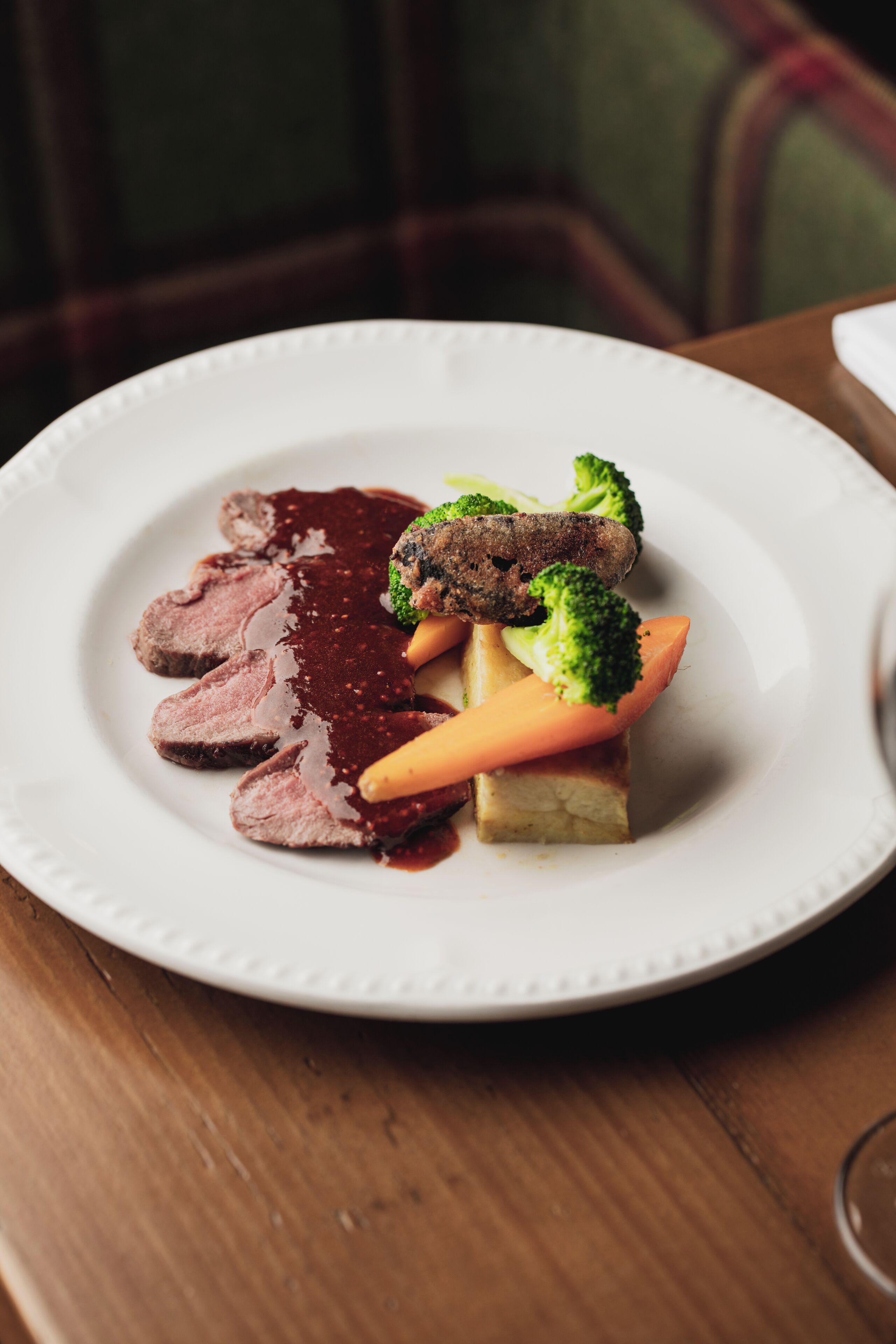 A plate of food with slices of meat, broccoli, and carrots.
