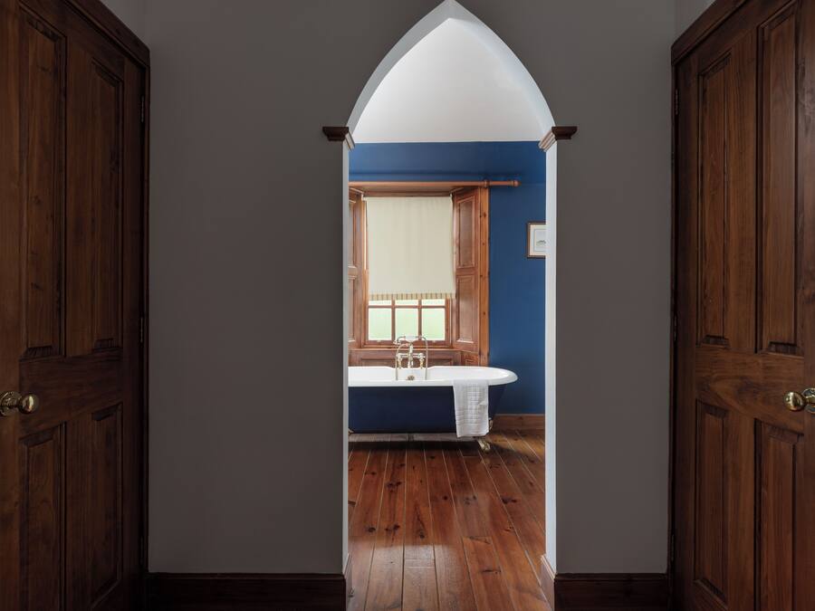 Een kamer met een houten vloer, een raam met een witte gordijn en een bad.