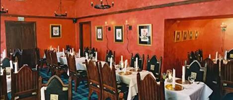 Un comedor con varias mesas y sillas, paredes rojas y cuadros enmarcados.