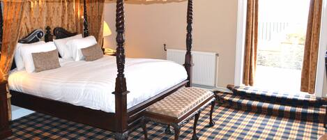 A four-poster bed with a bench, checkered carpet, and a view of the outdoors.