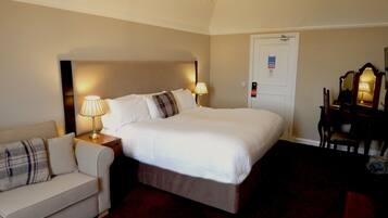 Habitación de hotel con una cama grande, una mesita de noche con lámpara, una silla, un escritorio con espejo y una puerta con letrero.