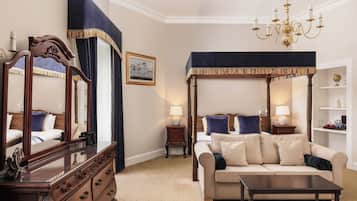 A well-appointed hotel room with a large bed, a sitting area with a sofa and armchair, a dresser, and a canopy bed.