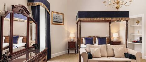 A well-appointed hotel room with a large bed, a sitting area with a sofa and armchair, a dresser, and a canopy bed.
