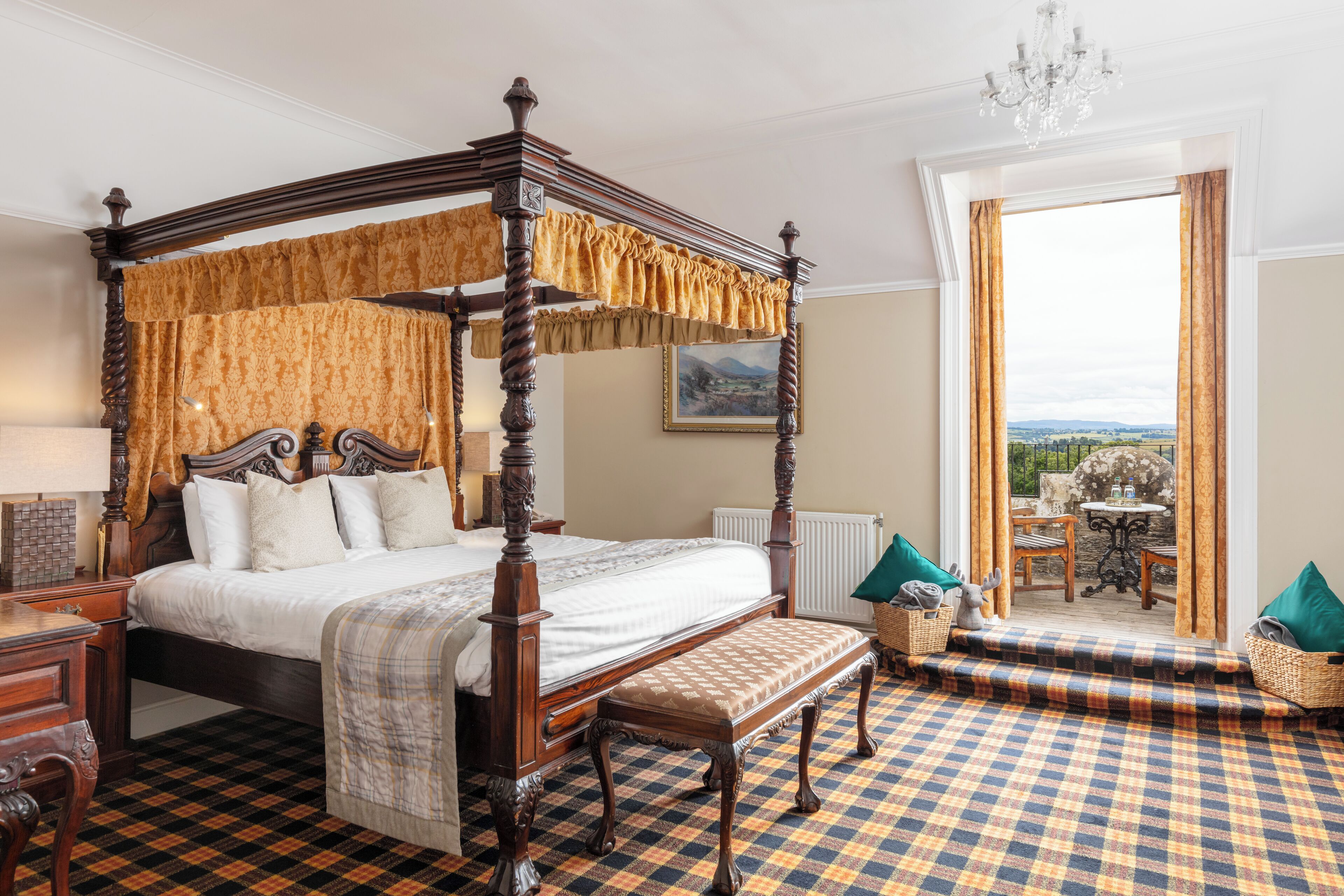 A four-poster bed with a bench, a checkered floor, a view through a window, and a chandelier.