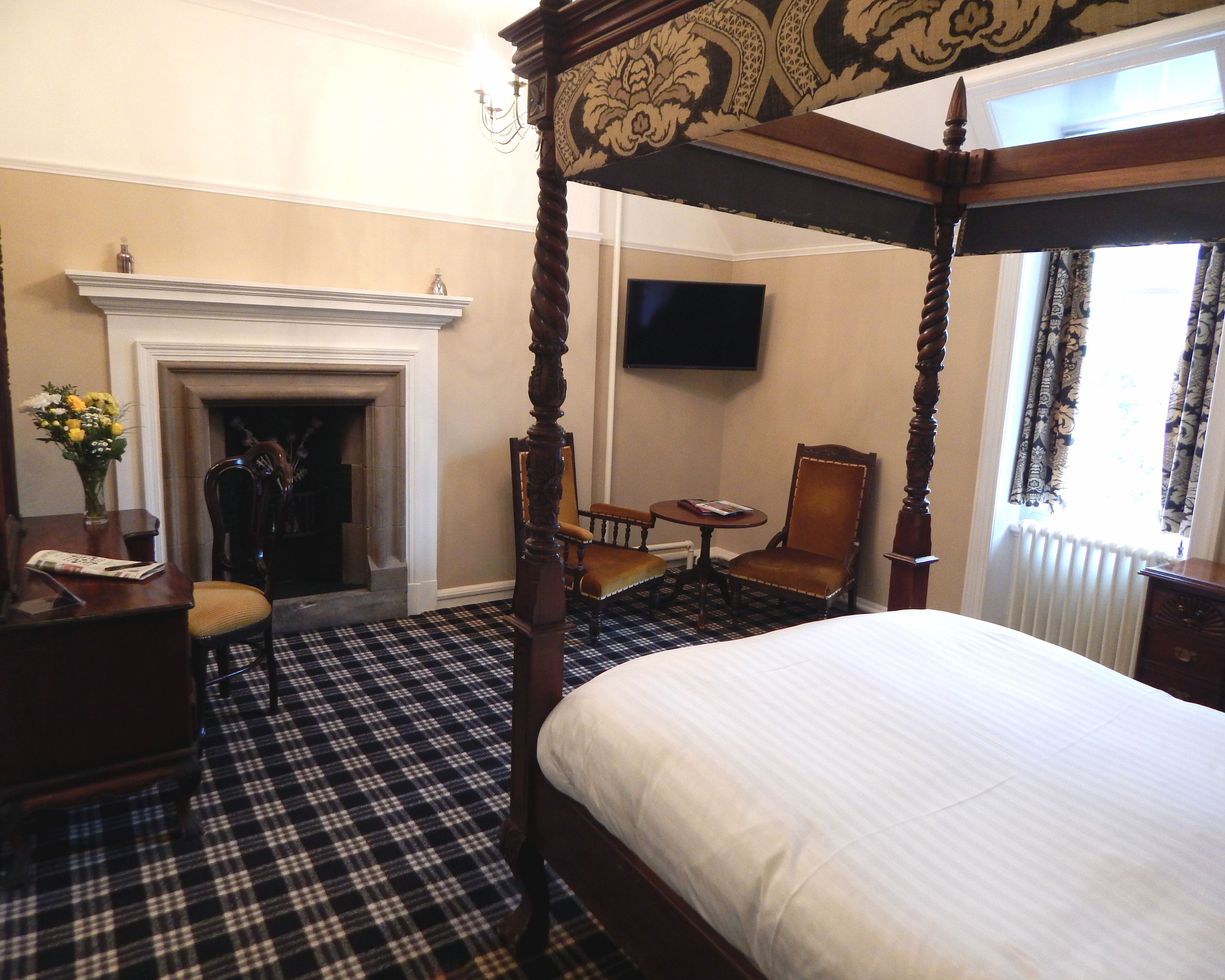 A hotel room with a four-poster bed, a fireplace, a television, and a checkered floor.