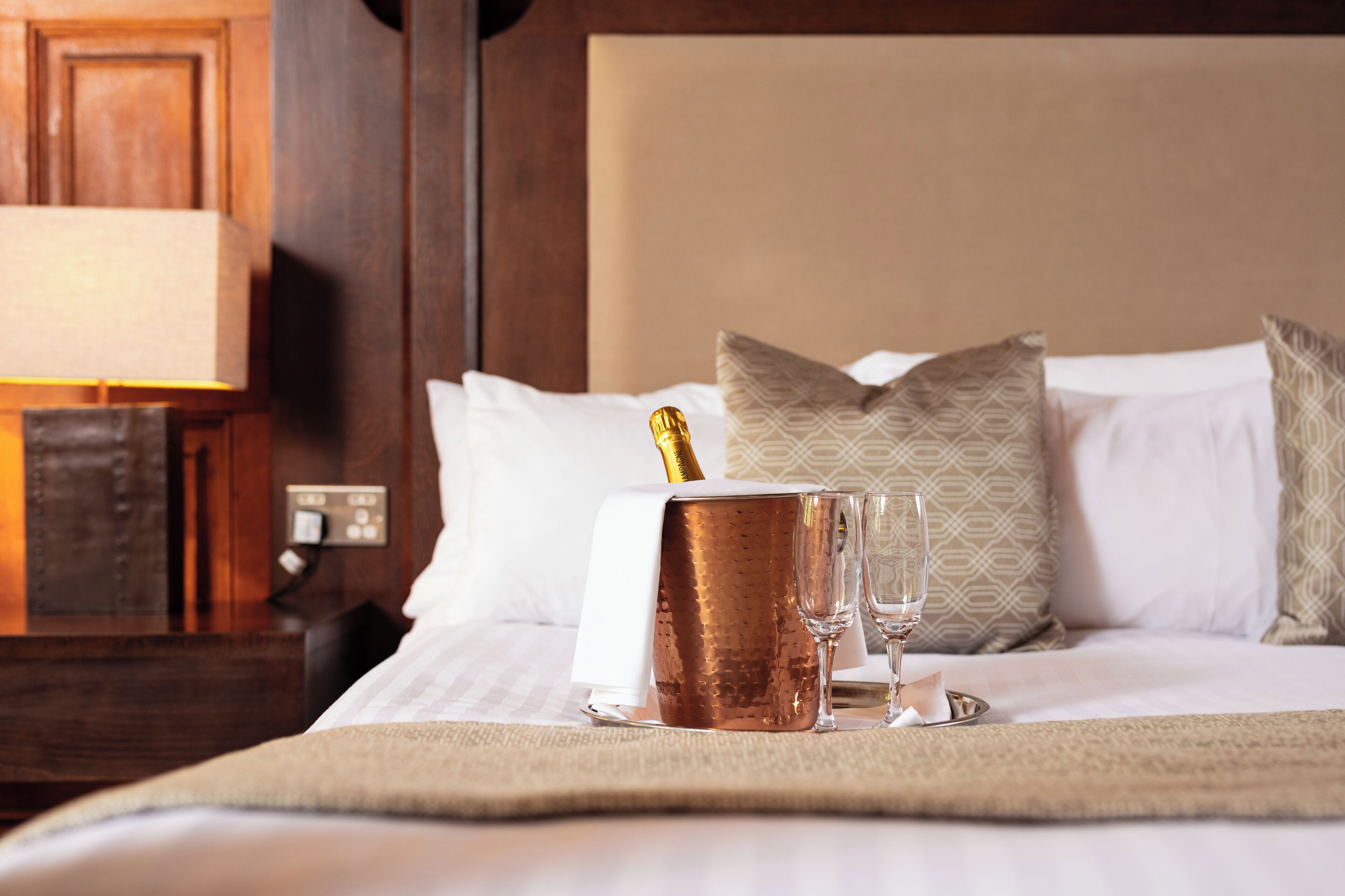 A neatly made bed with a champagne bottle, two glasses, and a tray.