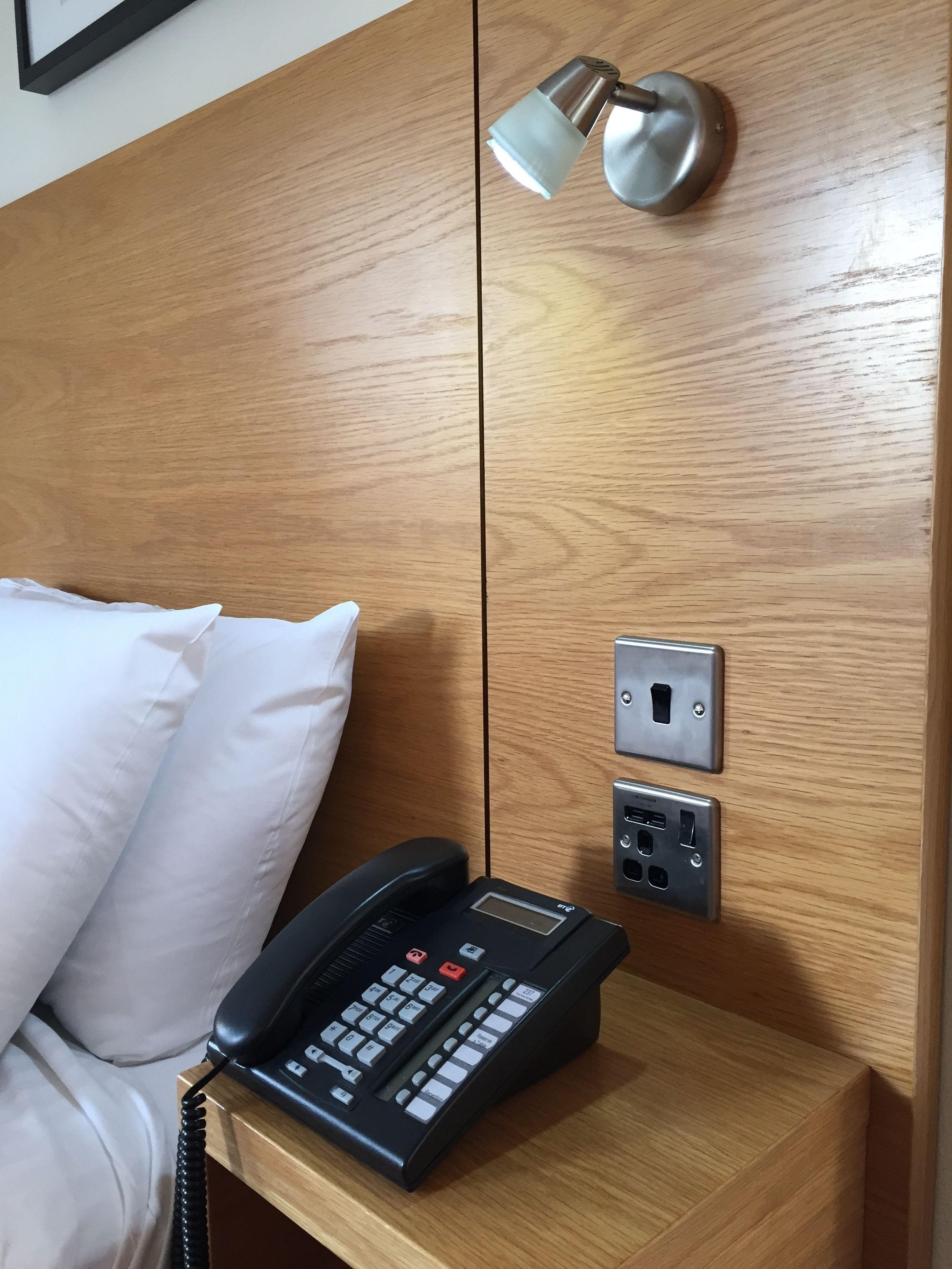 Una testiera in legno con un telefono, una presa elettrica e un portalampada.