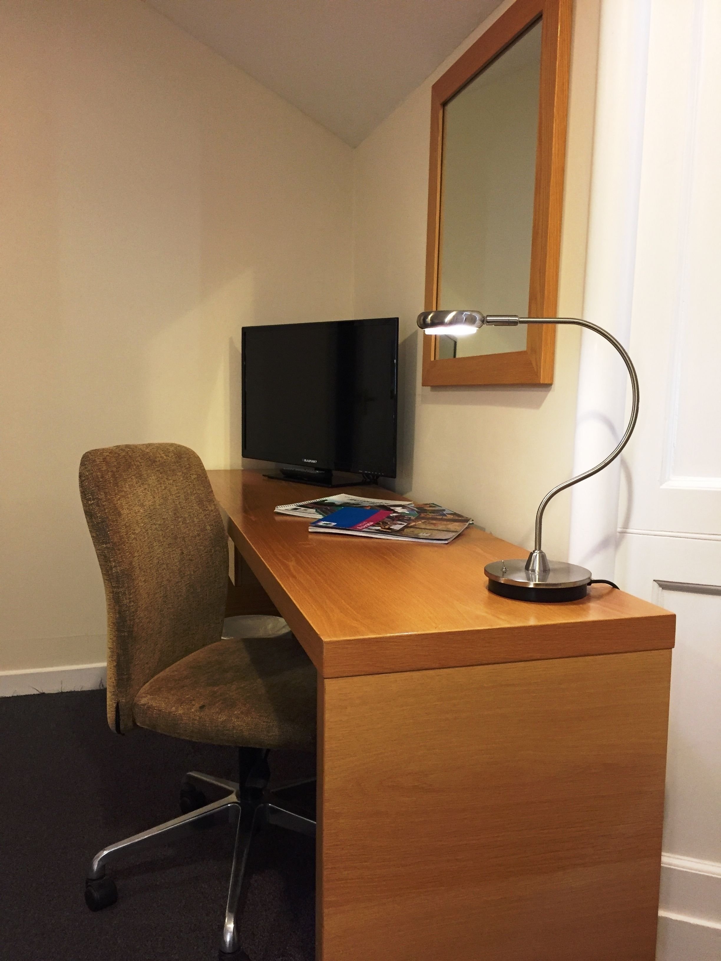 Una camera d'albergo compatta con una scrivania in legno, una televisione, una lampada da tavolo e una sedia.