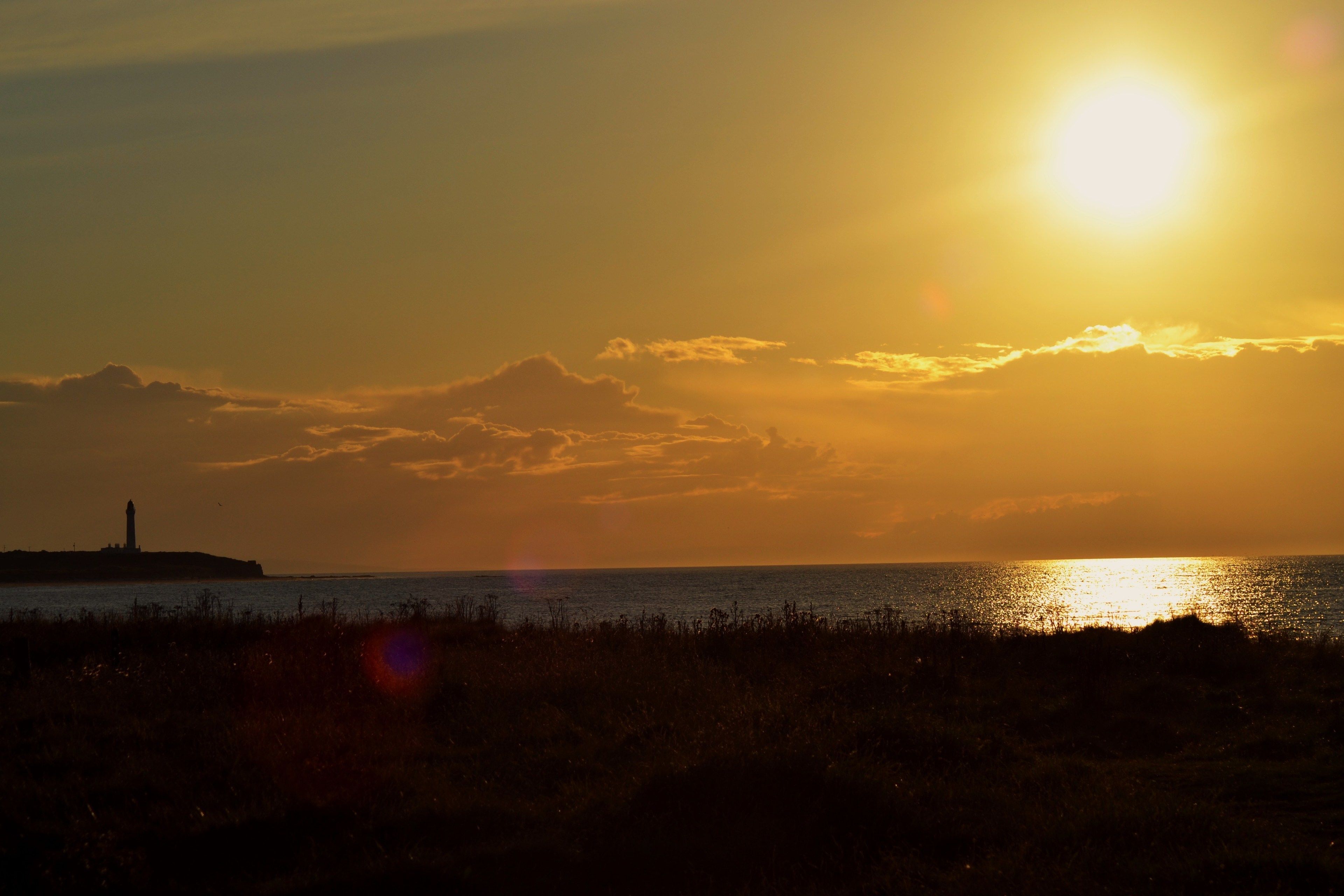A sunset over a body of water with a distant lighthouse.