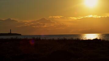 A sunset over a body of water with a distant lighthouse.