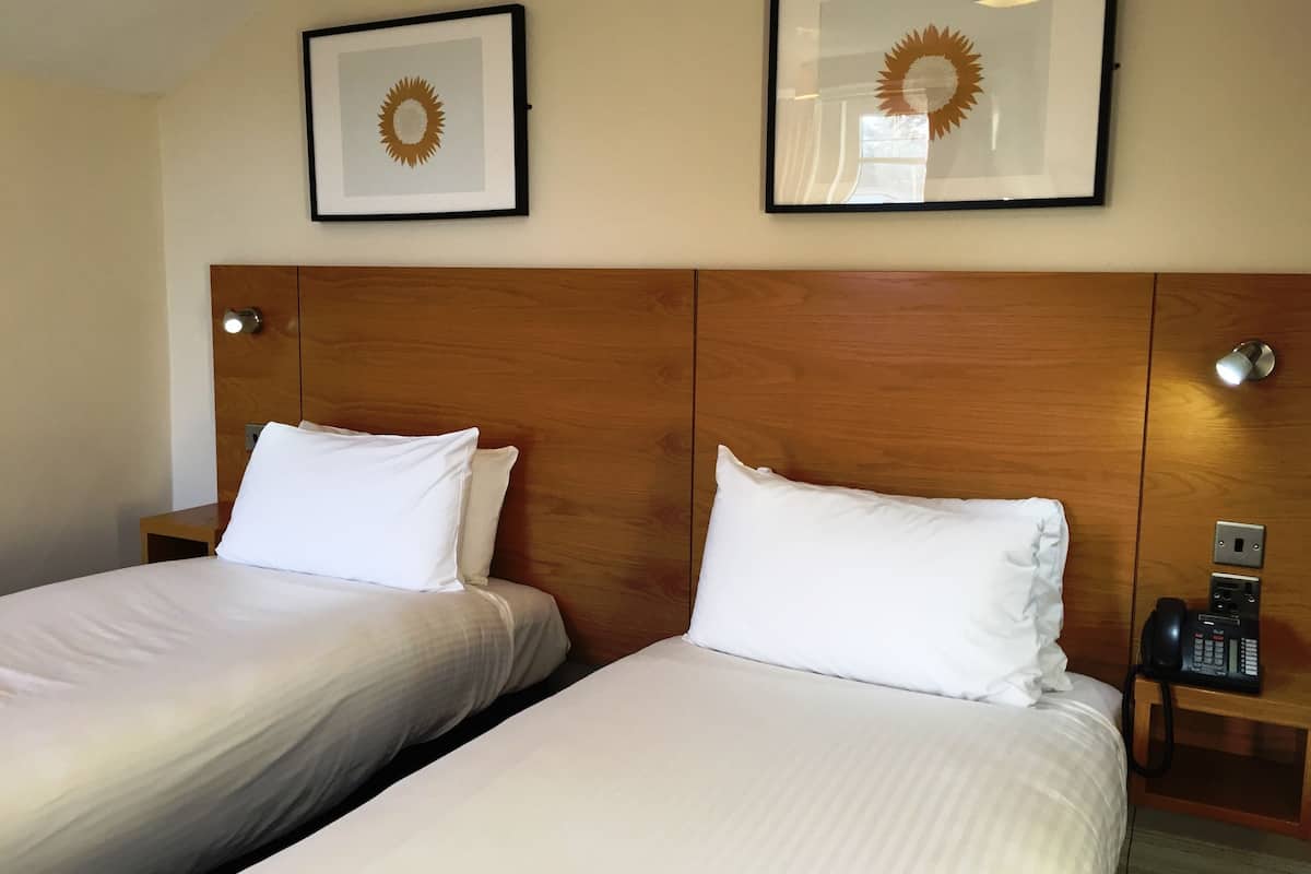 Une chambre d’hôtel avec deux lits, chacun agrémenté de draps et d’oreillers blancs, d’une tête de lit en bois et d’œuvres d’art encadrées au-dessus des lits.