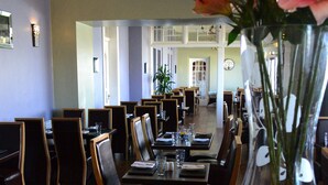 Un restaurante con una mesa larga, sillas y un florero con flores.