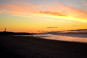A beach at sunset with a lighthouse silhouette.