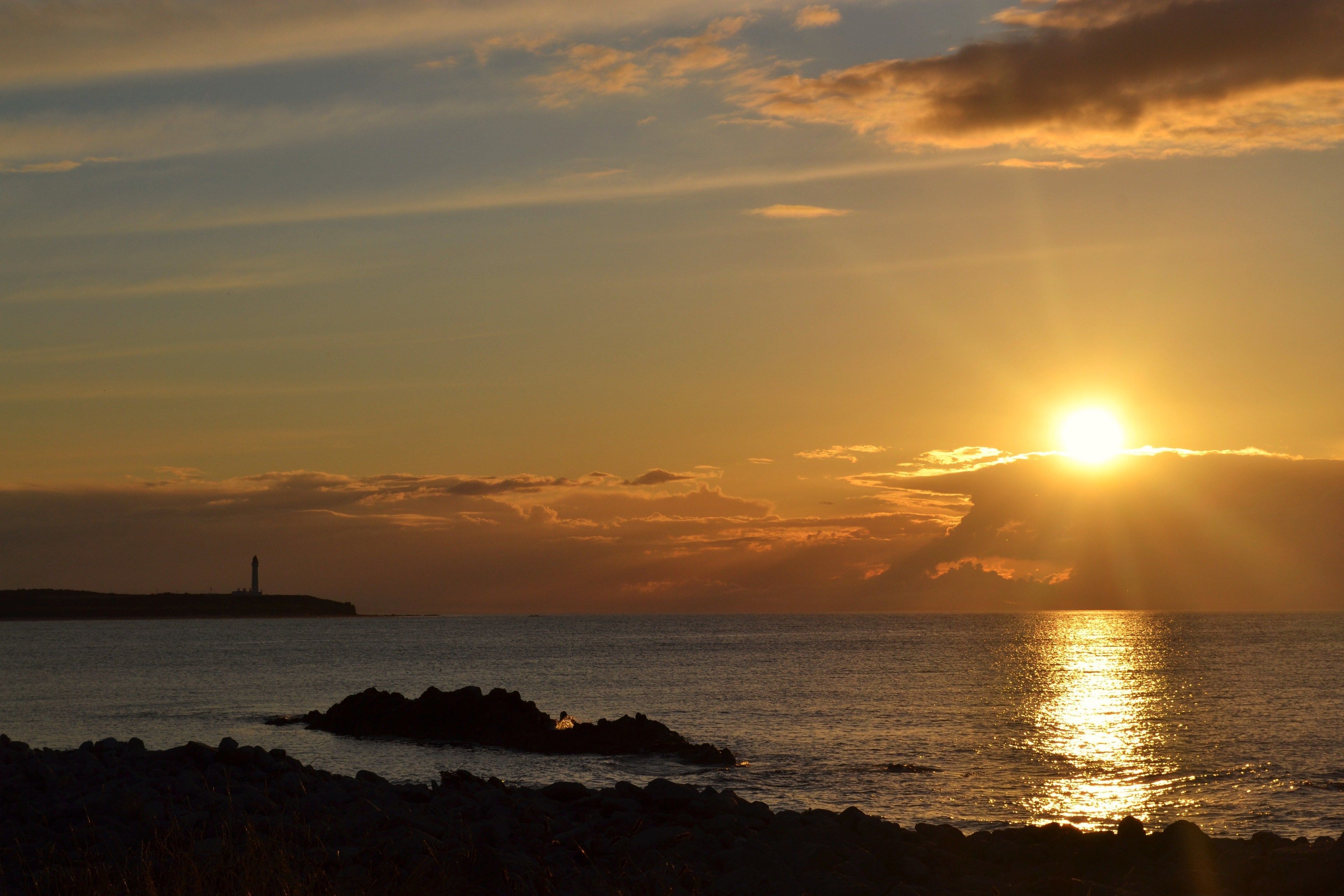 Un coucher de soleil sur une étendue d’eau, avec un phare visible au loin.