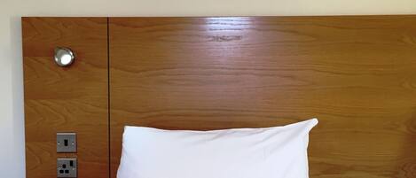 A neatly made bed with a wooden headboard, a bedside table with a lamp, and a framed picture on the wall.