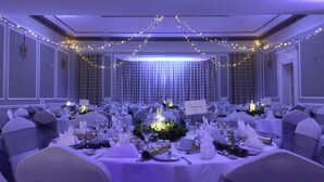 Un salón de banquetes con mesas redondas dispuestas para un evento formal, que incluye manteles blancos, cristalería y centros de mesa florales.