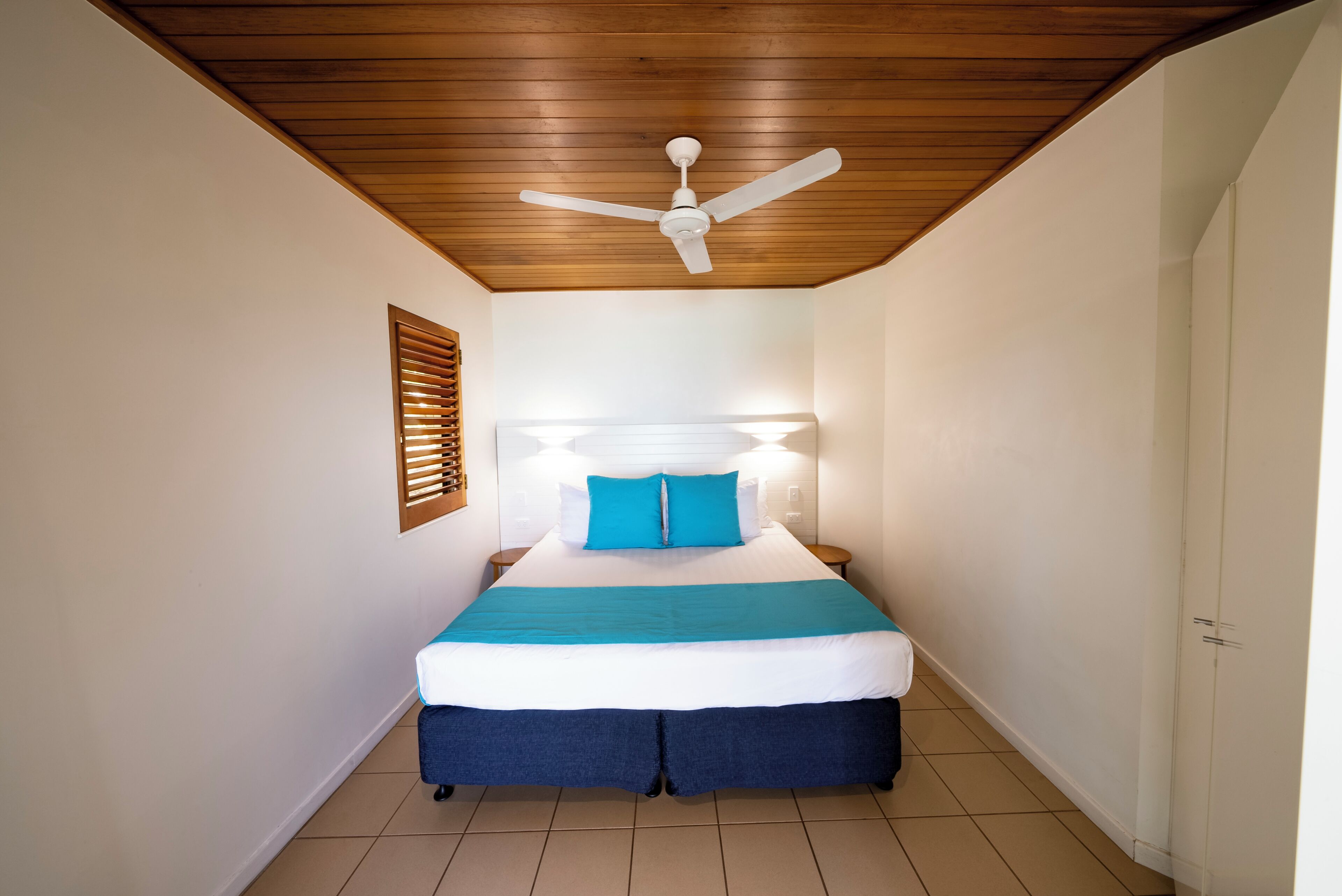 A bedroom with a wooden ceiling, a bed with a white headboard, blue bedding, and a ceiling fan.