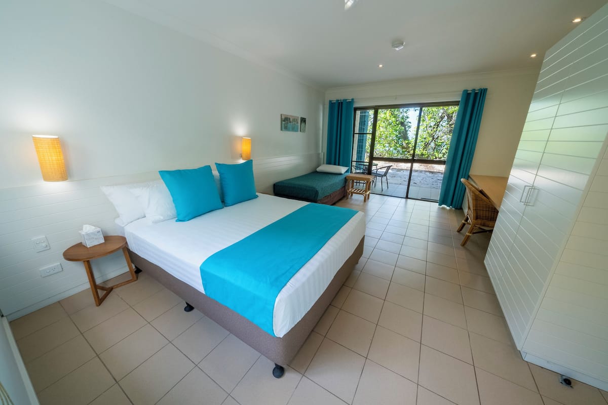 A hotel room with a bed, a small table, a chair, and a view of the outdoors through a glass door.
