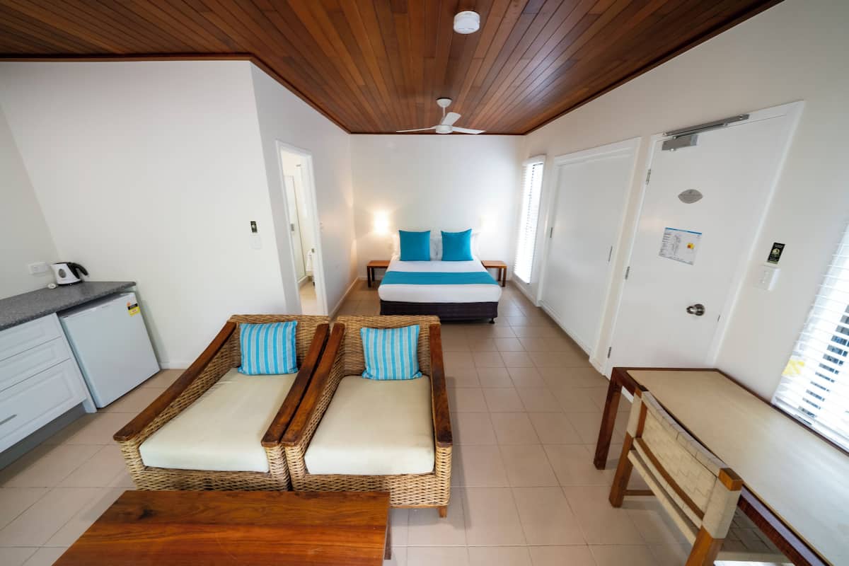 A room with a bed, two wicker sofas, a wooden table, and a ceiling fan.
