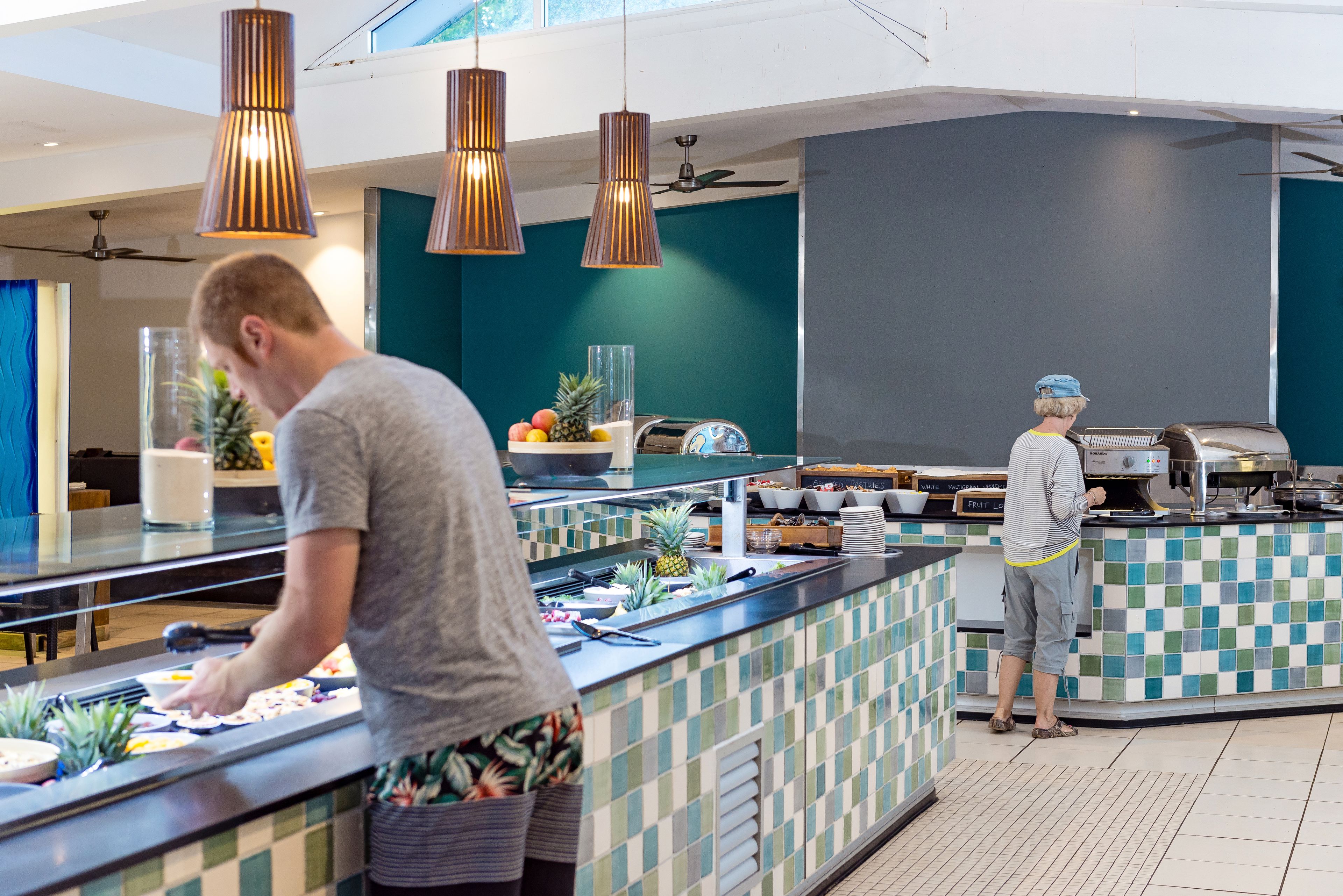 A buffet area with a counter, various food items, and two people serving.