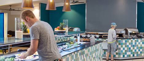 Zona de buffet con un mostrador, diversos alimentos y dos personas atendiendo.