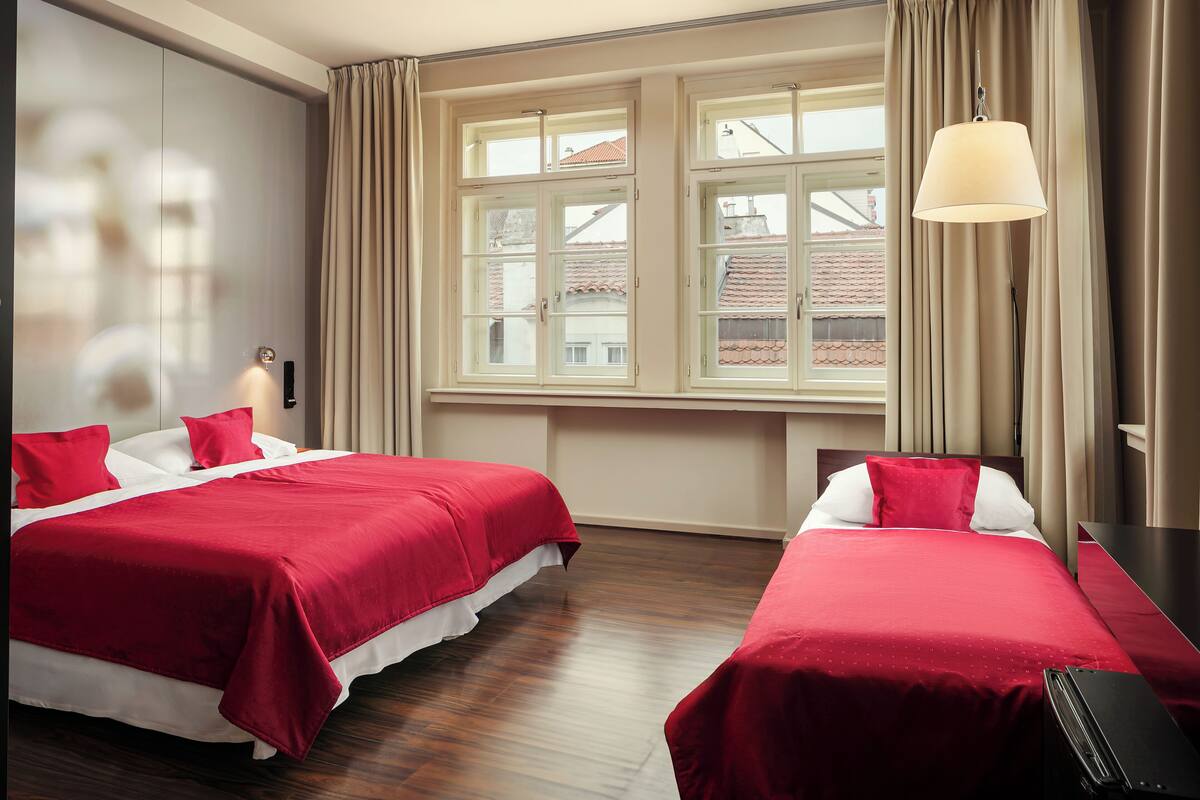 A hotel room with two beds, a large window with curtains, a desk, and a lamp.