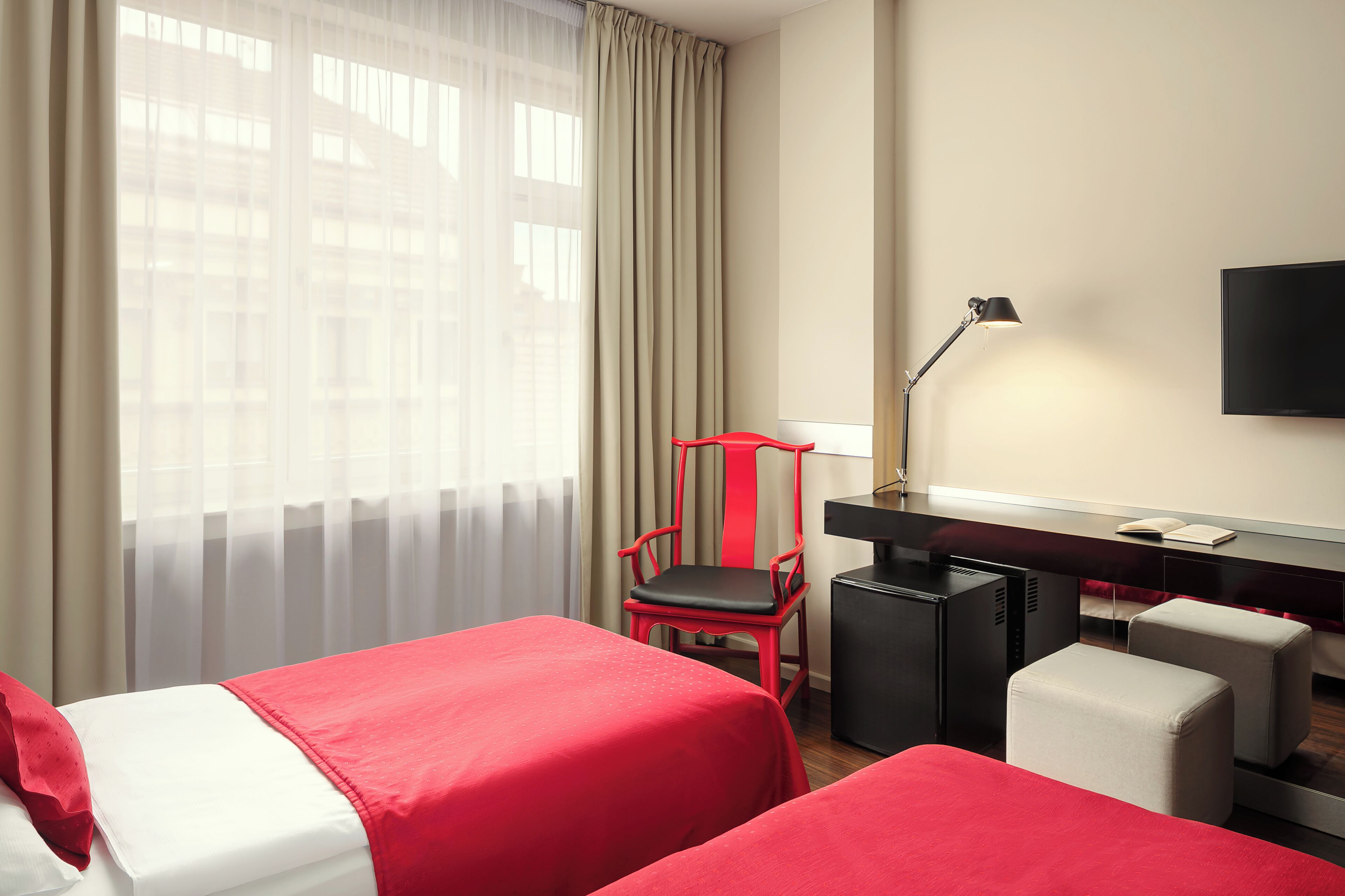 Ein Hotelzimmer mit zwei Betten, einem Schreibtisch, einem Sessel, einem Fernseher und einem Fenster mit Vorhängen.