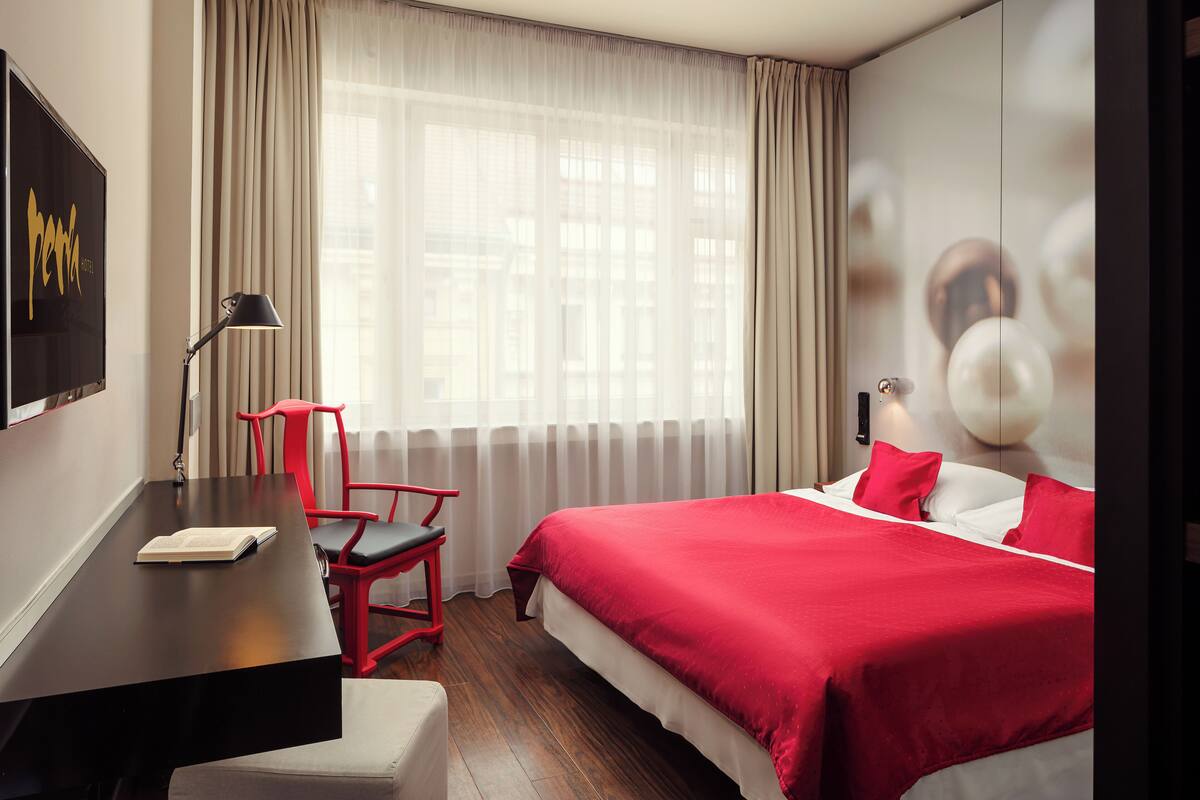 A hotel room with a bed, a desk, a chair, and a large window with curtains.
