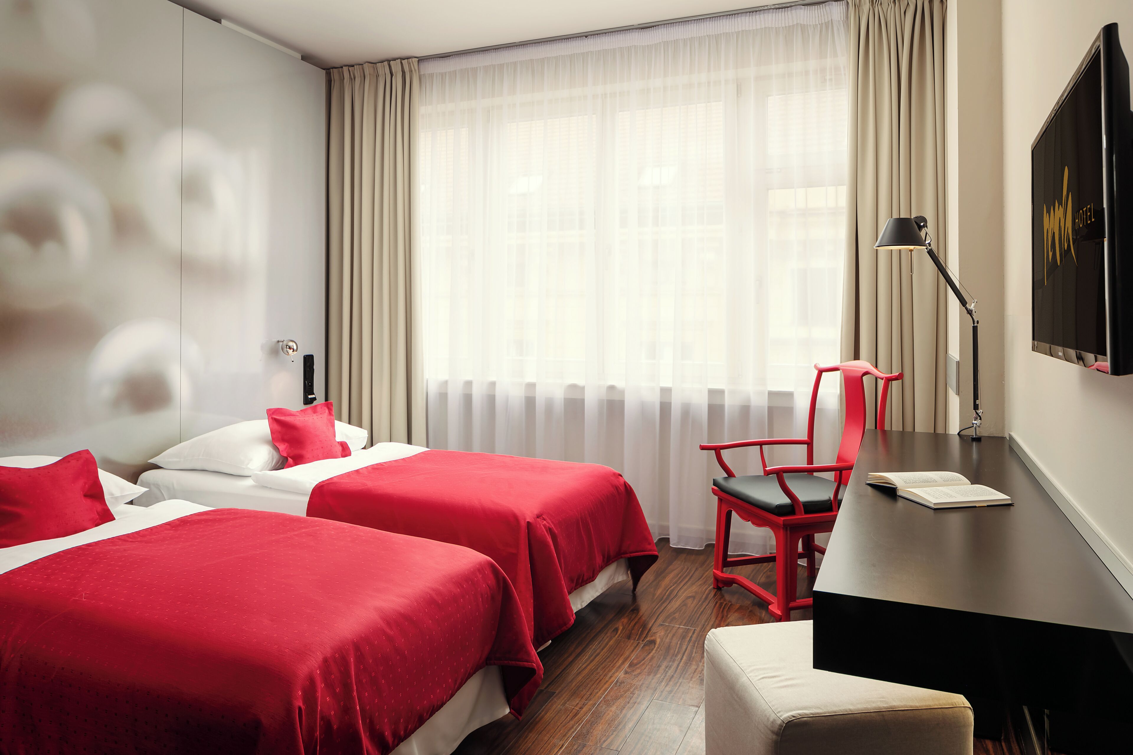 Habitación de hotel con dos camas, un escritorio, una silla y un amplio ventanal con cortinas.