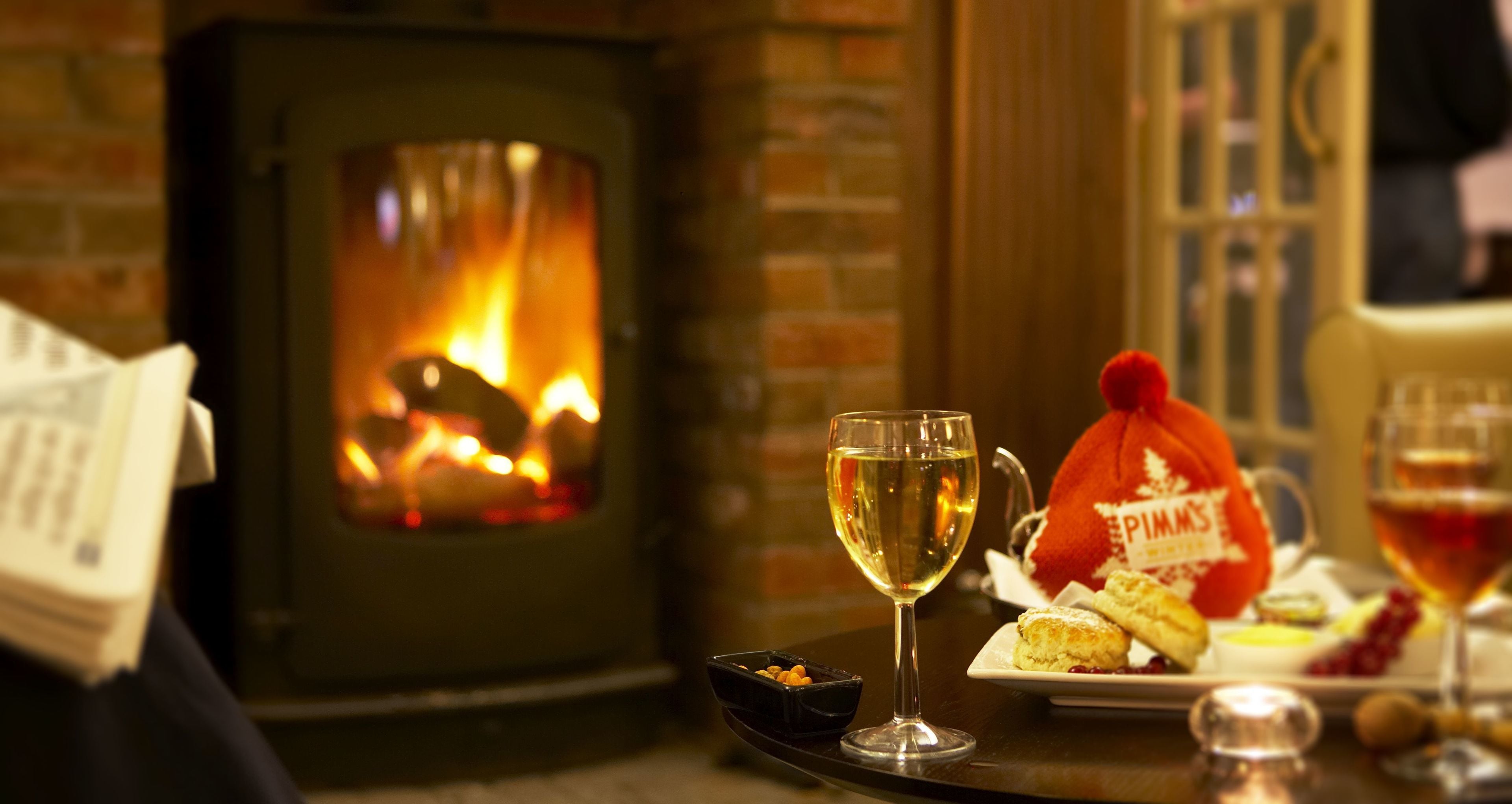 Una habitación acogedora con chimenea, un plato de scones y dos copas de vino.