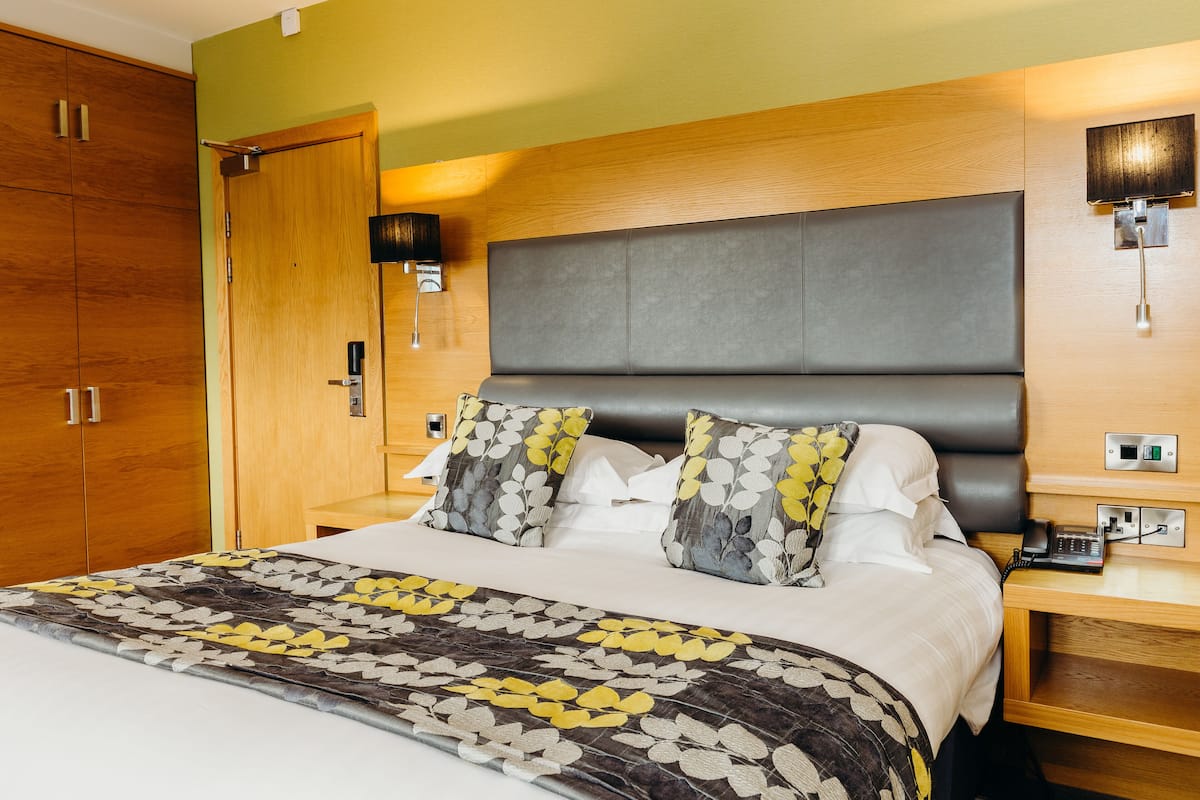 Habitación de hotel con cama, armario de madera, mesita de noche y lámpara de pared.