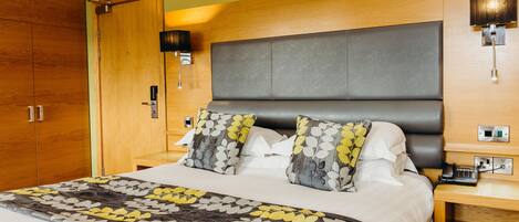 Une chambre d’hôtel comprenant un lit, une armoire en bois, une table de chevet et une lampe fixée au mur.