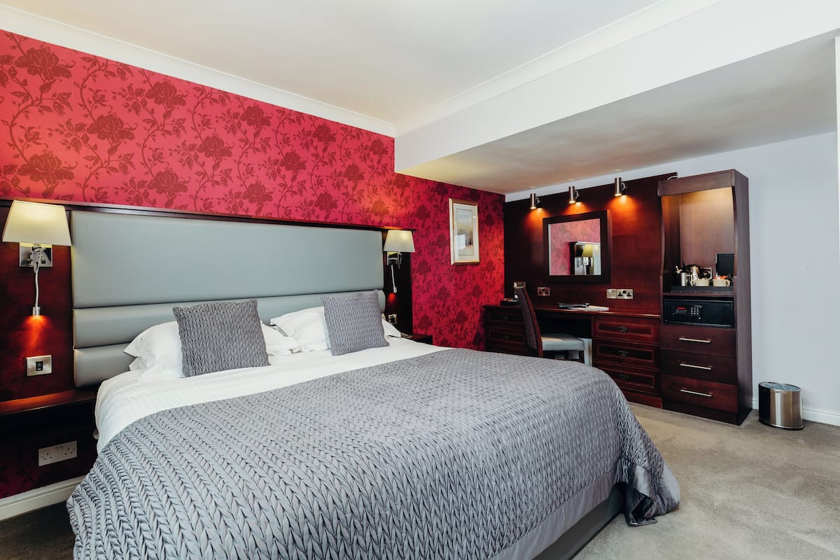Un dormitorio con una cama grande, un aparador, un espejo y un papel tapiz floral rojo.