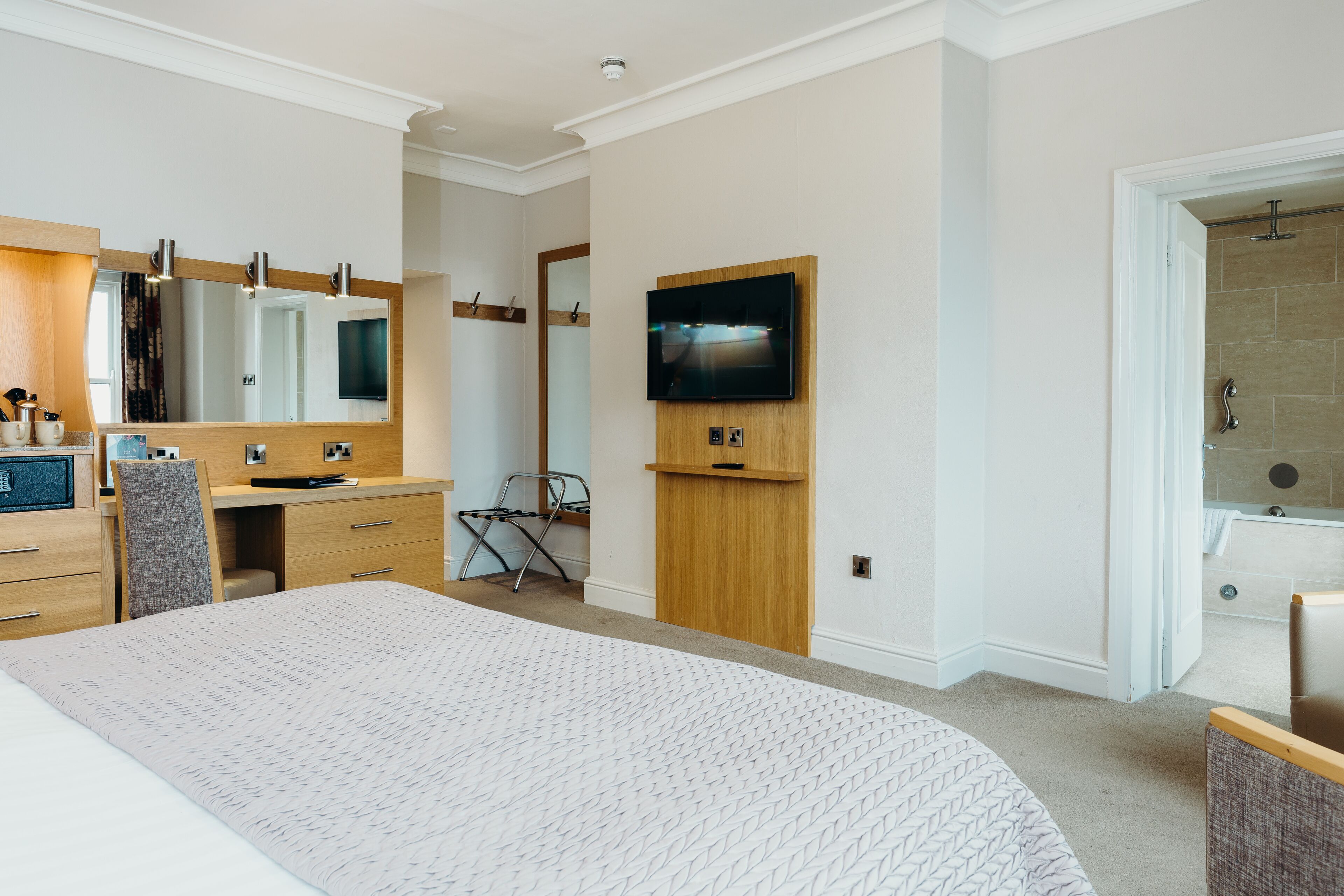 A modern hotel room with a large bed, a desk, a chair, a TV mounted on the wall, and a shower area.