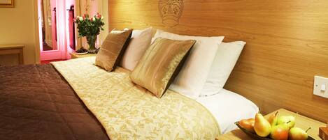 A neatly made bed with a floral bedspread, a bedside table with a fruit bowl, and a wooden headboard with a crown design.