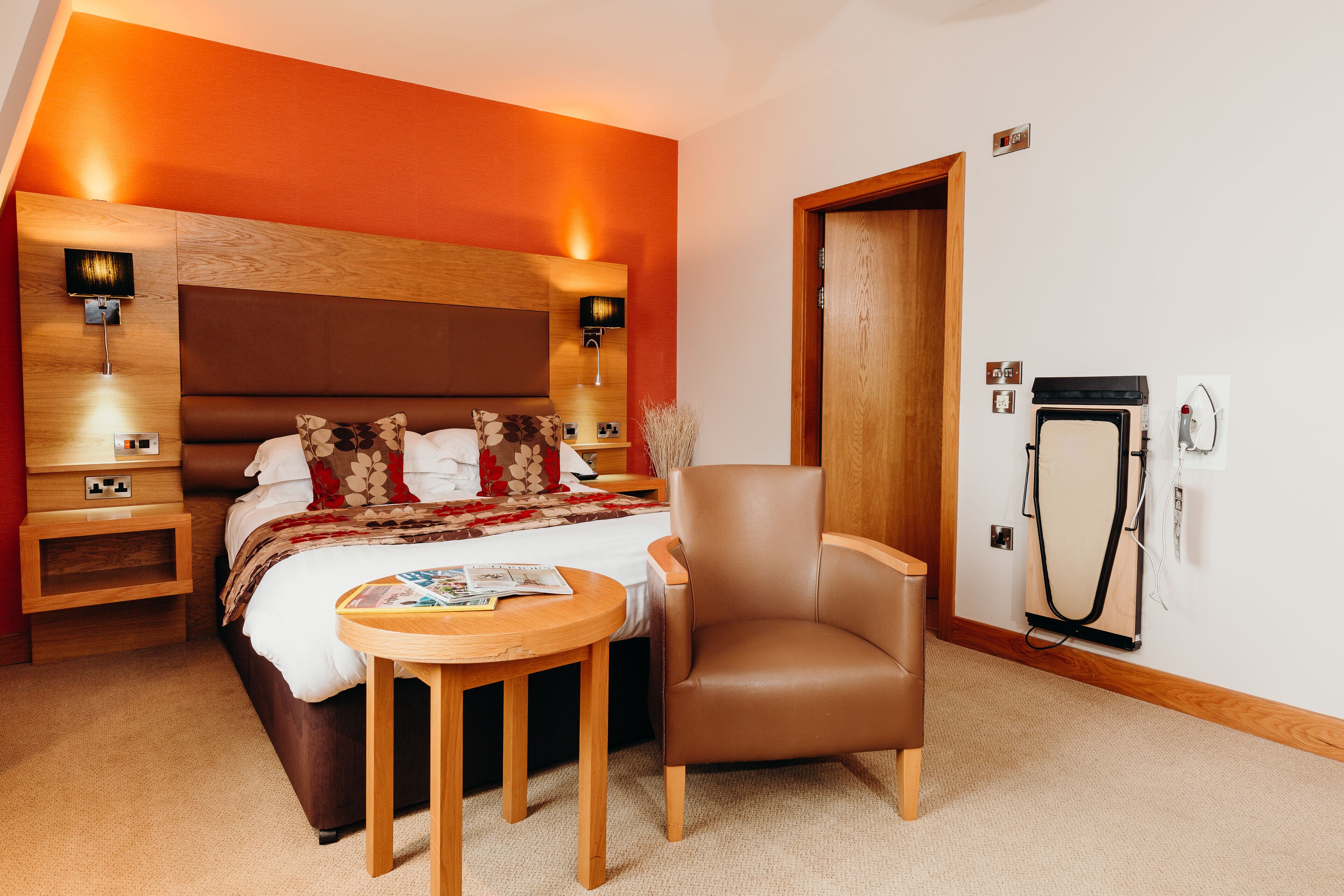 A hotel room with a bed, a chair, a table, and a wall-mounted heater.
