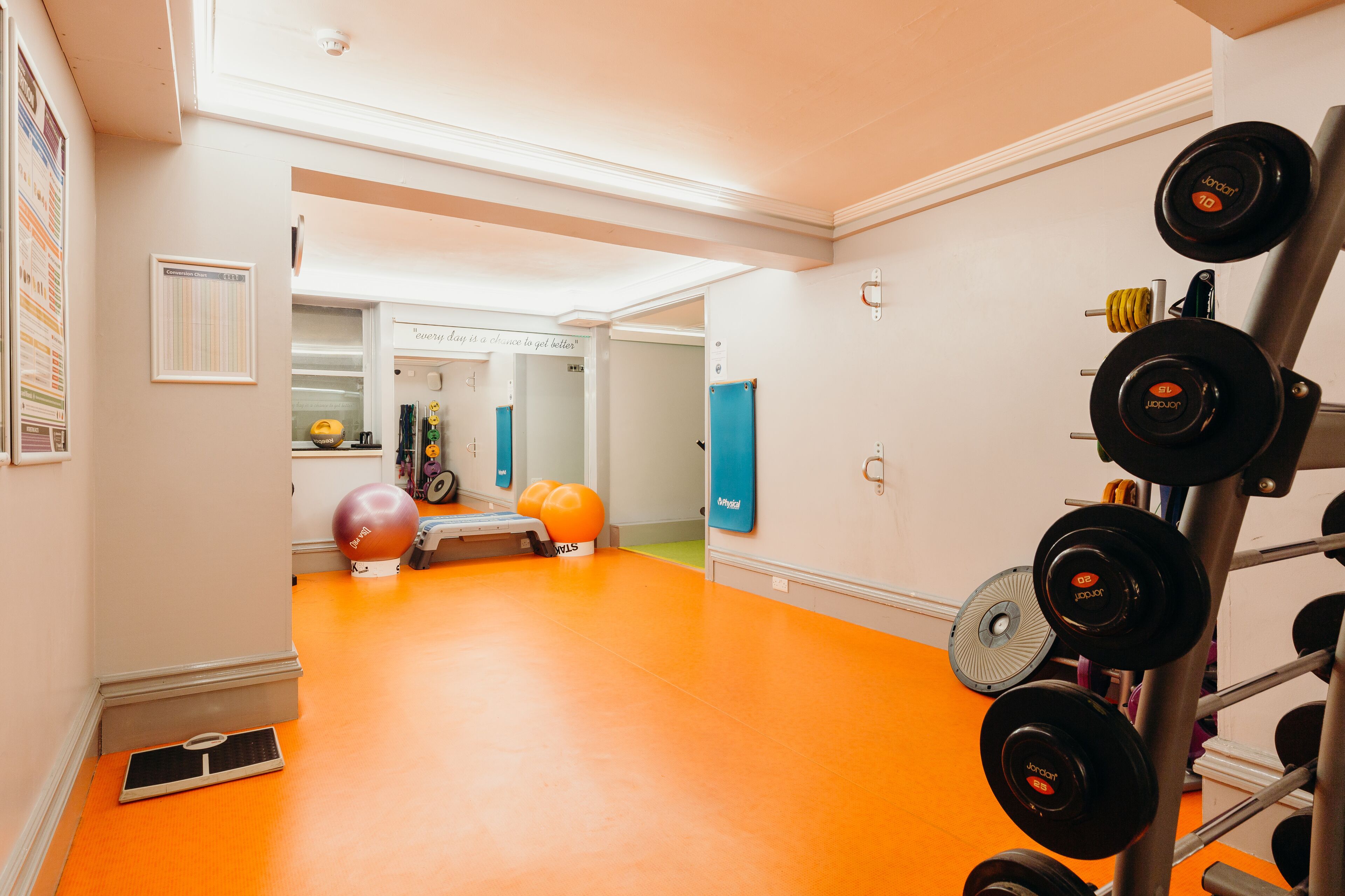 A gym with orange flooring, a weight rack, exercise balls, and a mirror.
