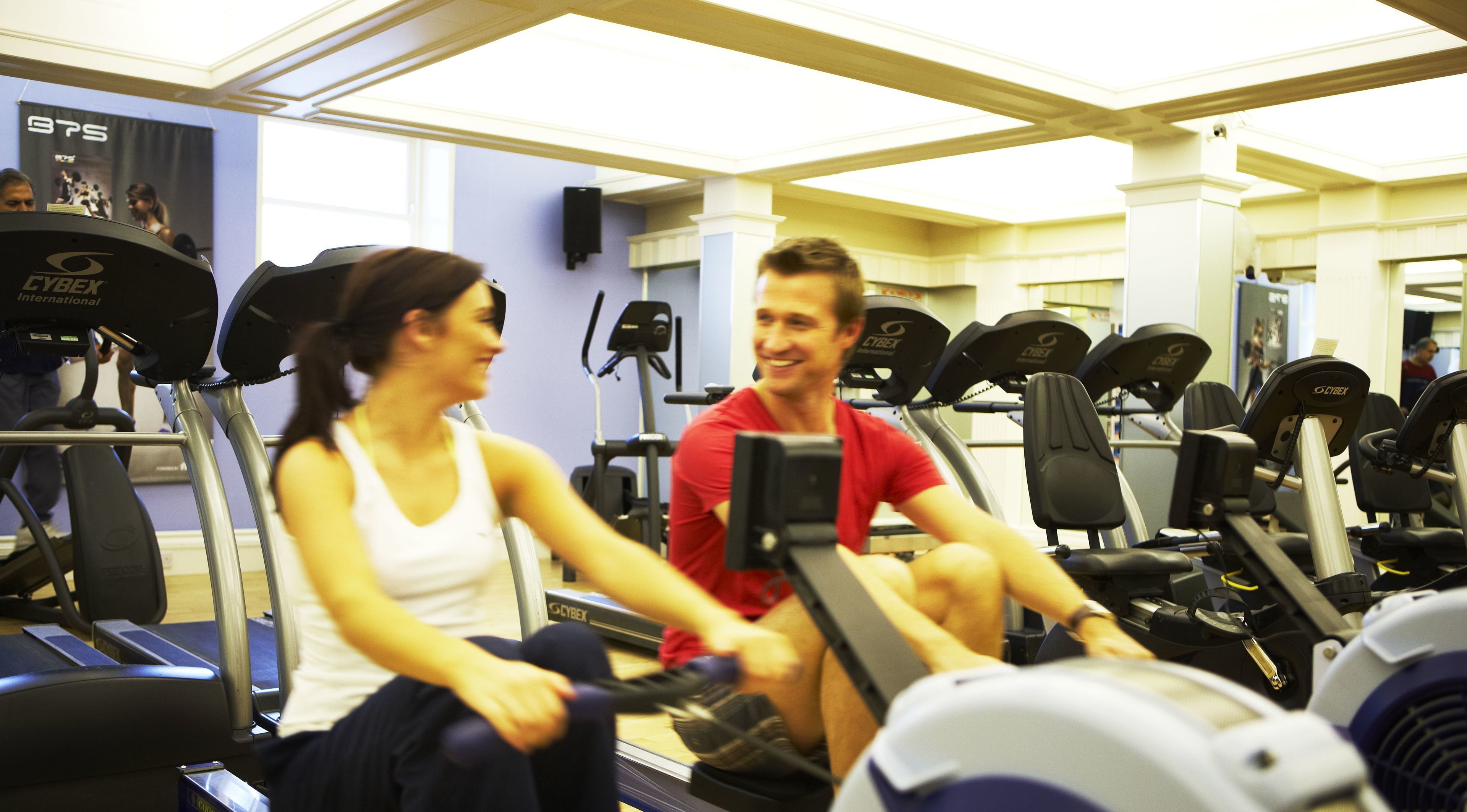 Een sportschool met hometrainers, krachtapparaten en een banner met de tekst 'BTS'.