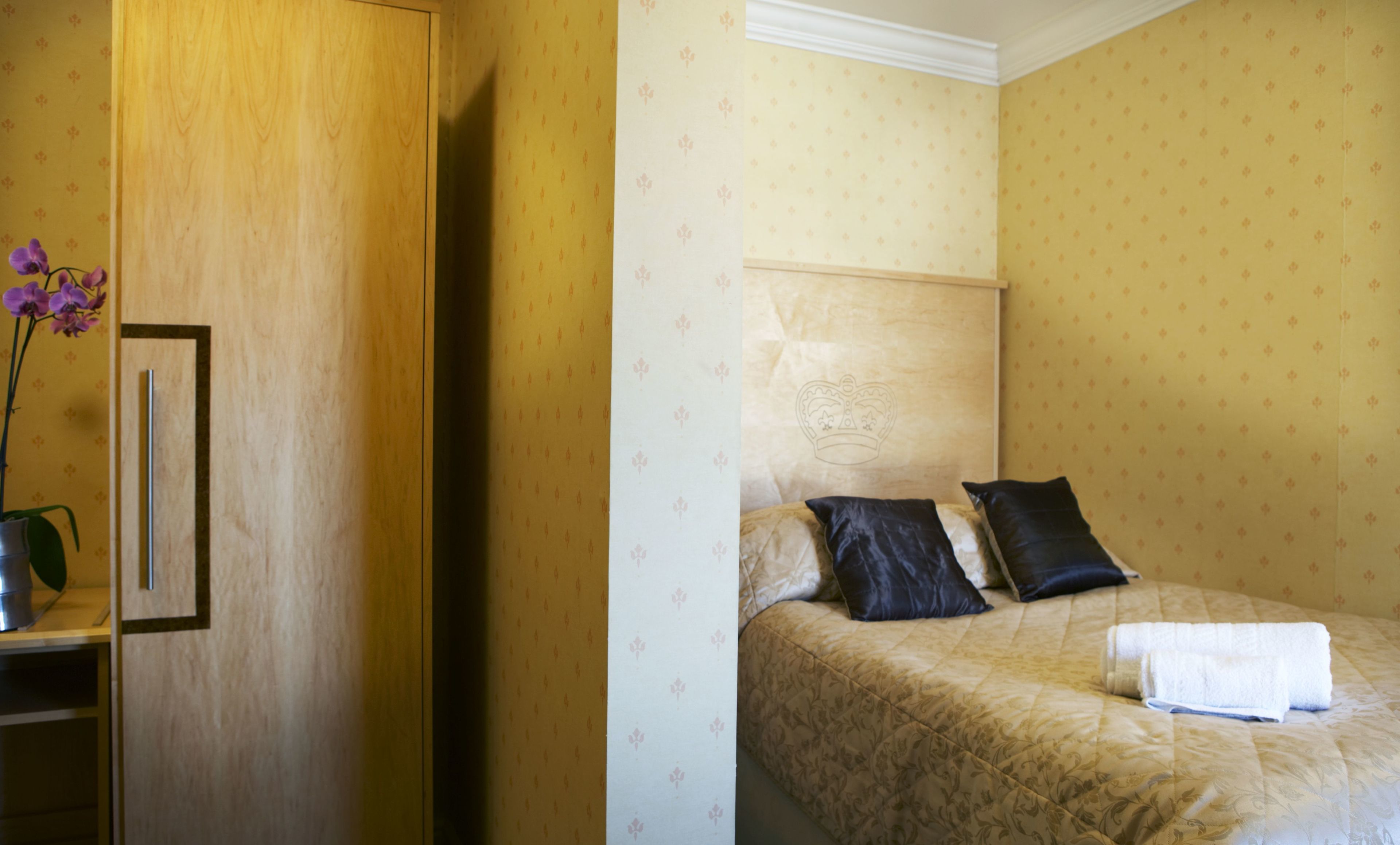 A hotel room with a bed, pillows, a nightstand, and a vase with flowers.