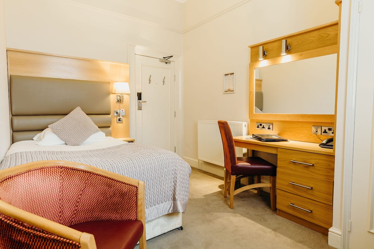 Habitación de hotel con cama, escritorio, silla y un espejo grande.