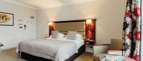 A hotel room with a large bed, bedside lamps, a chair, and a table with magazines.