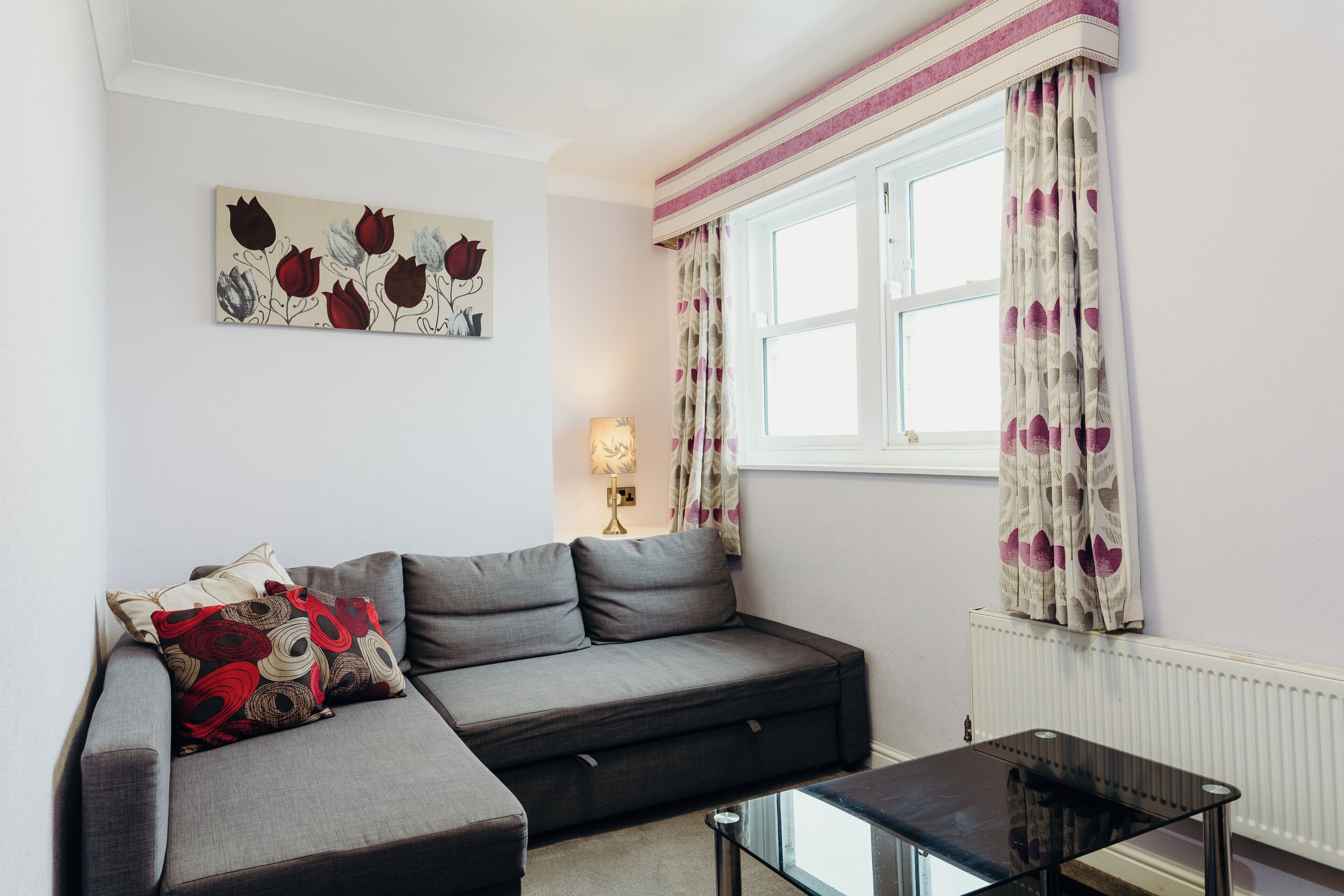 A modern living room with a grey sofa, a glass coffee table, and a painting on the wall.