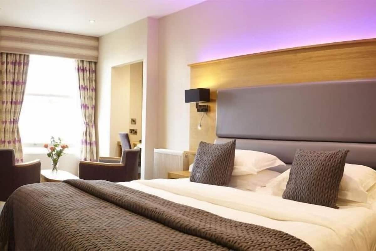 Habitación de hotel con una cama grande, mesitas de noche, una silla, un escritorio y una ventana con cortinas.