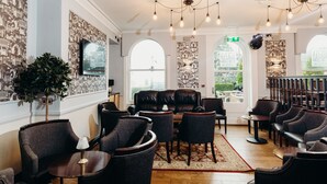 A modern lounge with leather sofas, dark chairs, and a central coffee table. Large windows provide natural light and views of the outdoors.
