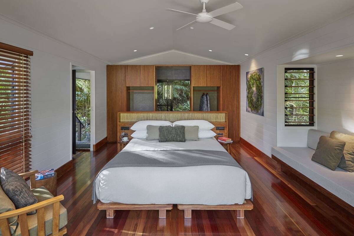 A modern bedroom with a large bed, wooden paneling, and a ceiling fan.