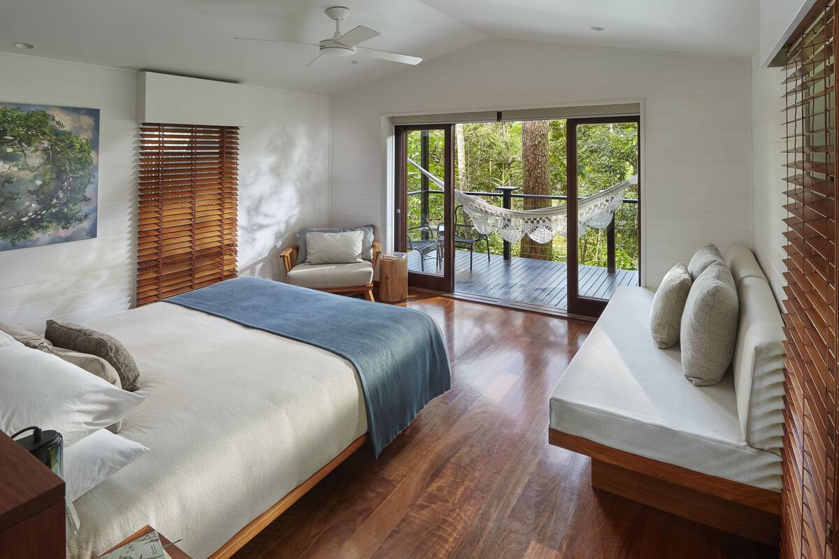 A bedroom with a large bed, a sofa, a chair, and a view of the outdoors.