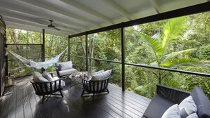 A covered outdoor deck with wooden flooring, two cushioned chairs, a hammock, and a sofa with pillows. - Silky Oaks Lodge, Beckons (Finlayvale)